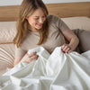 Smiling woman enjoying the soft and protective Duratherme Waterproof Quilt. Designed for durability and moisture resistance, this waterproof bedding offers ultimate comfort while safeguarding against spills and allergens. Ideal for a clean, modern bedroom aesthetic.