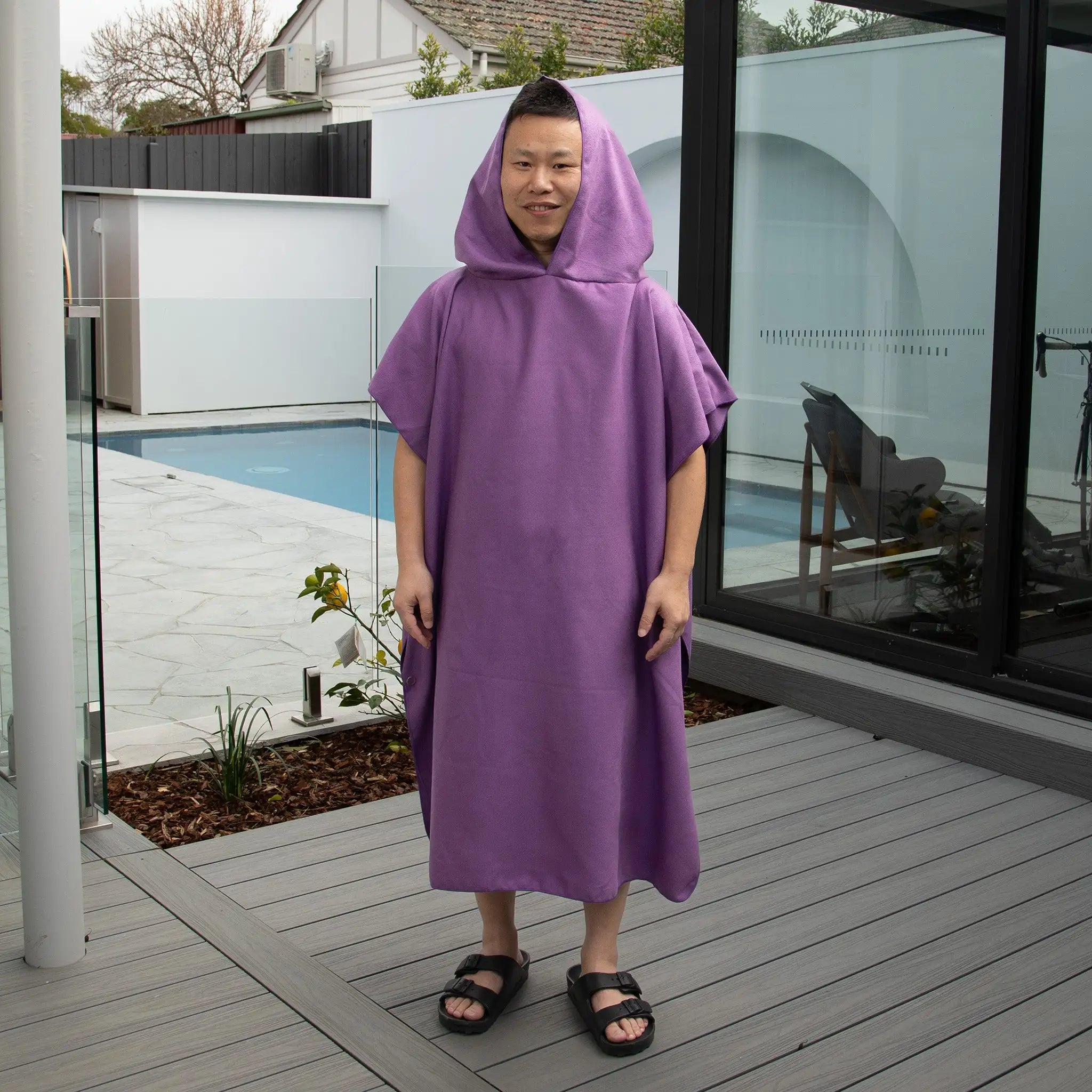 Adult wearing StayDry microfibre hooded poncho towel in purple. Ultra-absorbent, lightweight, and quick-drying towel, perfect for beach, swimming, and travel.