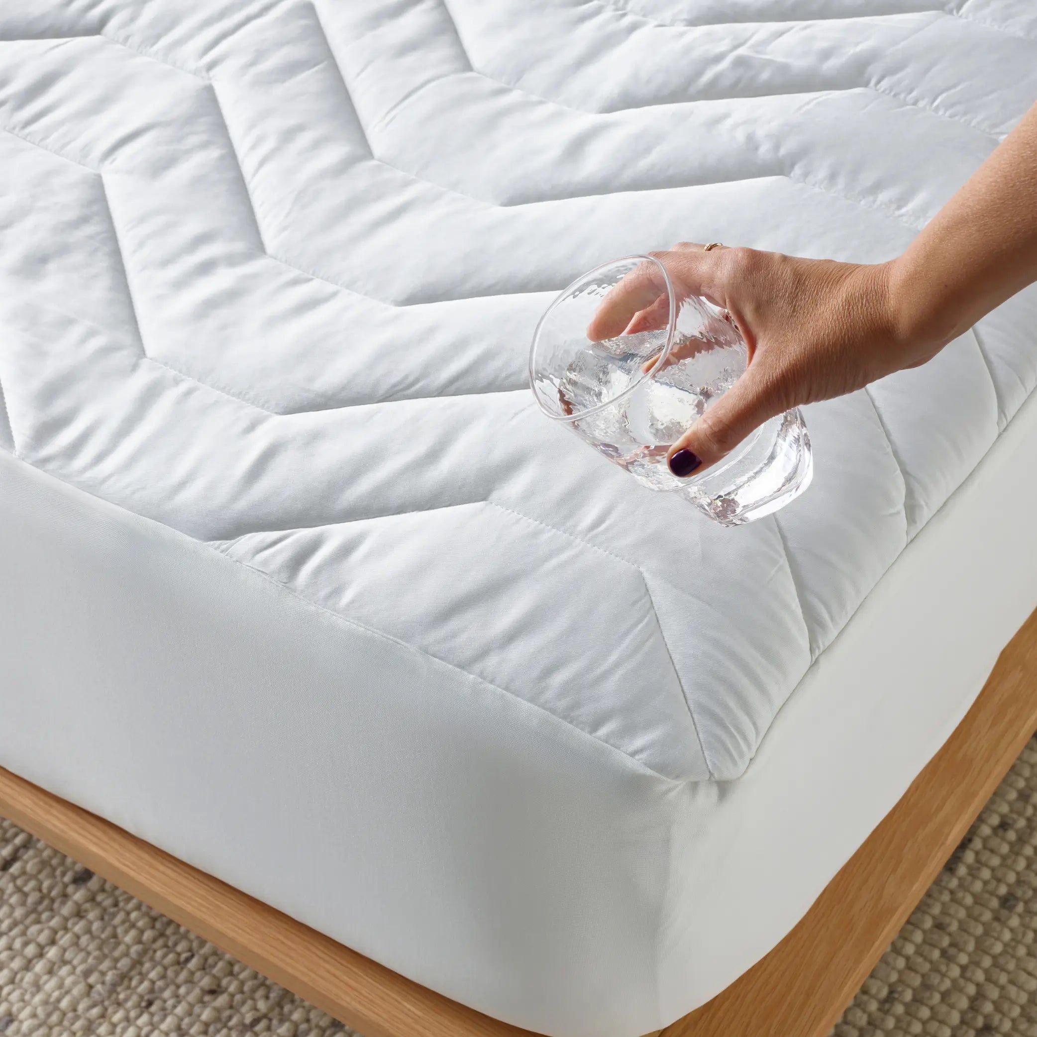 Hand pouring water onto a waterproof bamboo mattress protector, demonstrating its liquid-resistant and breathable fabric. This hypoallergenic, soft, and durable mattress cover provides protection against spills, allergens, and dust mites, ensuring a clean and comfortable sleep environment.